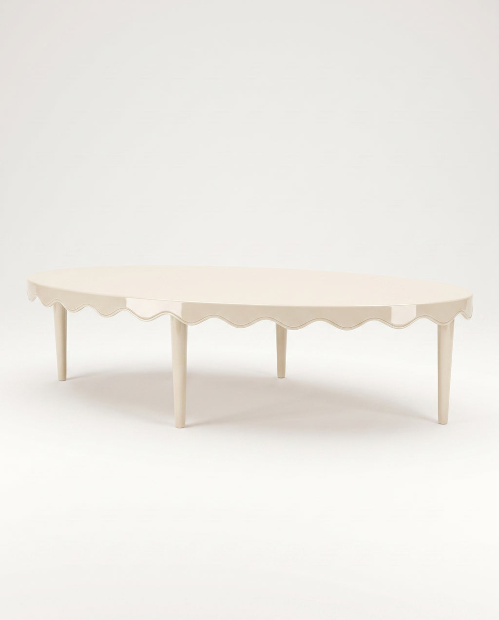 Romance oval coffee table in off-white lacquer with scalloped apron and tapered legs, Monde Singulier Editions, three-quarter view