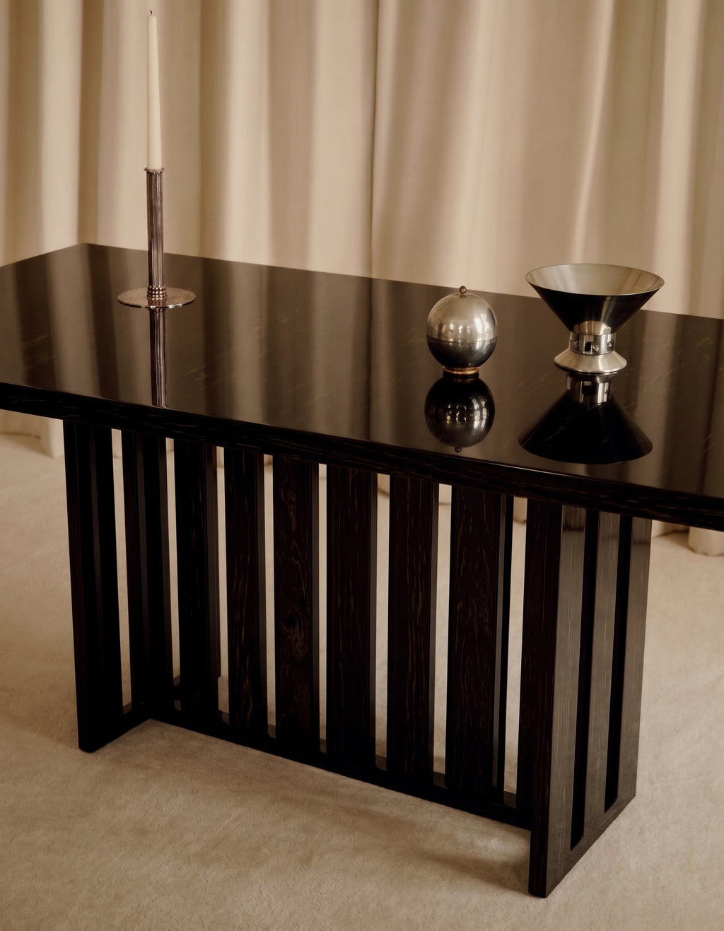 Table à manger Cardinal en laque noire, piètement à lattes, dressée avec un bougeoir et des objets en métal, Monde Singulier Editions