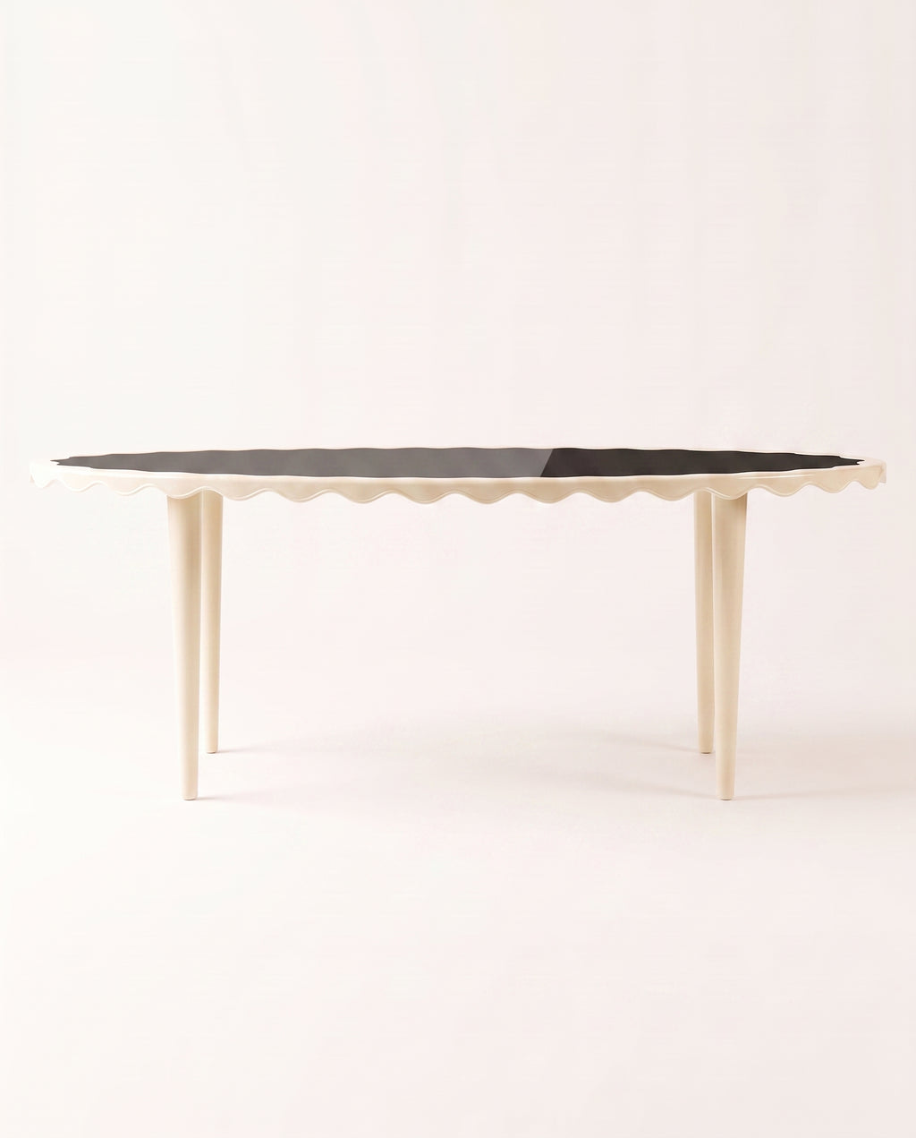 Romance oval dining table with black lacquer top, off-white scalloped apron and tapered legs, Monde Singulier Editions, three-quarter view