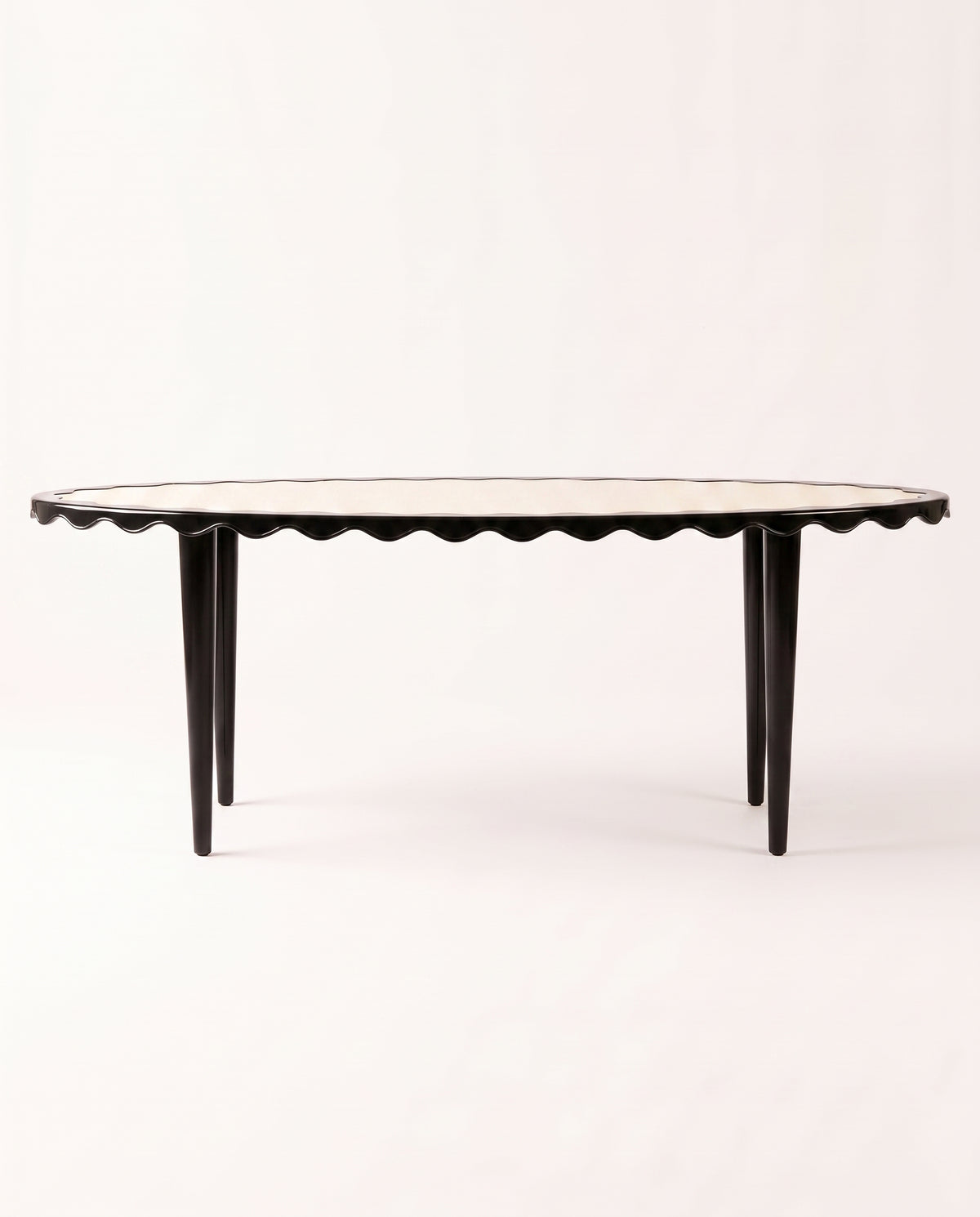 Romance oval dining table in black lacquer with scalloped apron and tapered legs, Monde Singulier Editions, three-quarter view