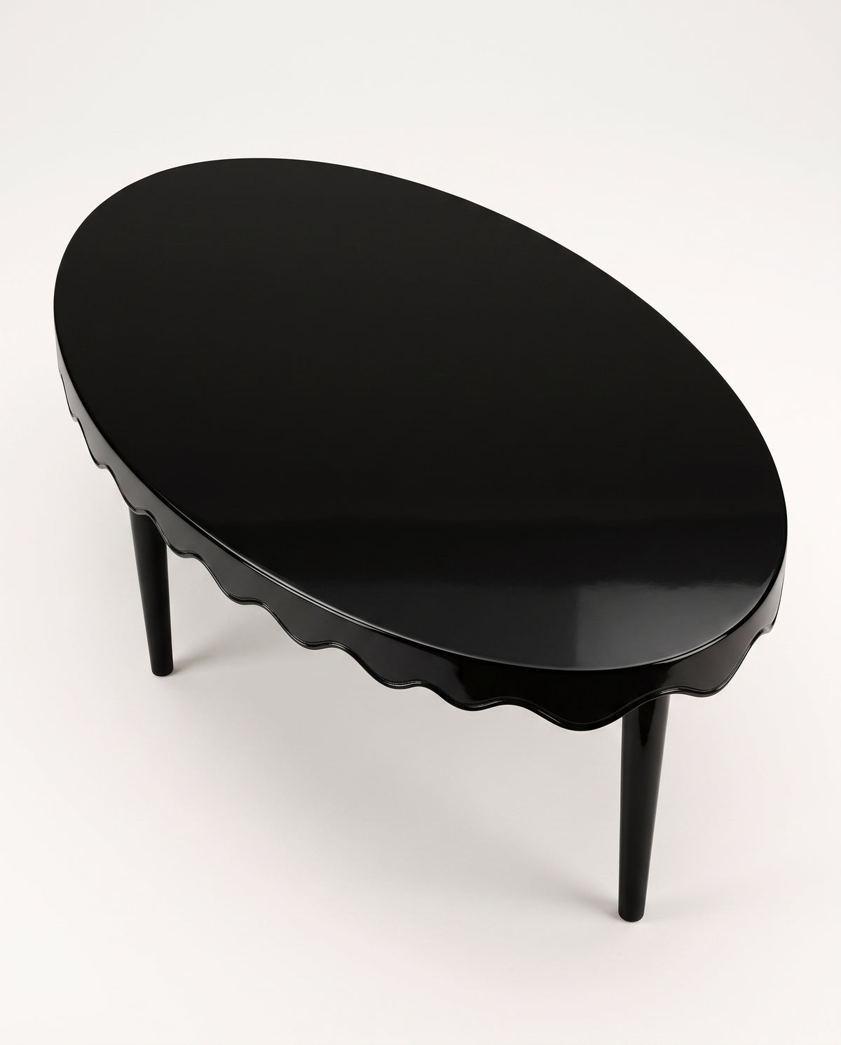 Romance oval coffee table in black lacquer, elevated view of the glossy top and scalloped edge, Monde Singulier Editions